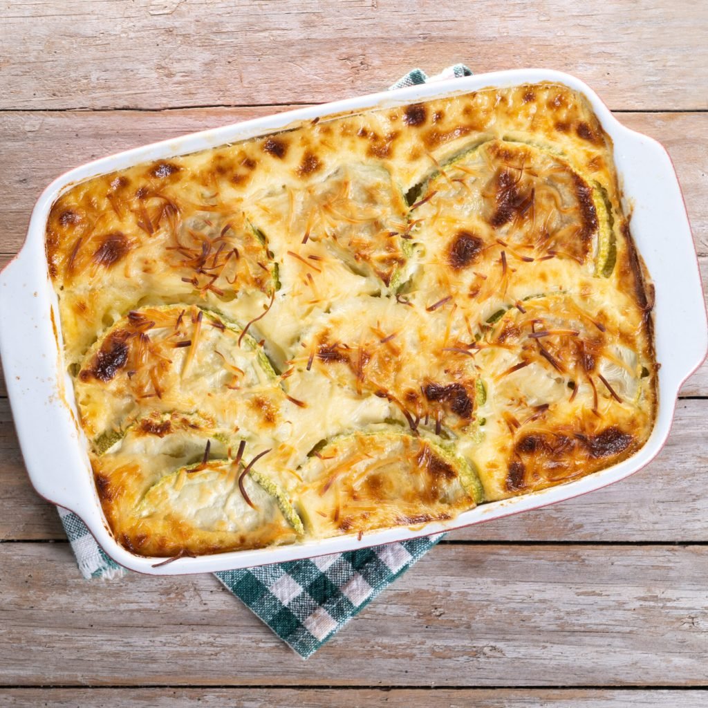 Casserole with cheese and gratin zucchini on wooden table