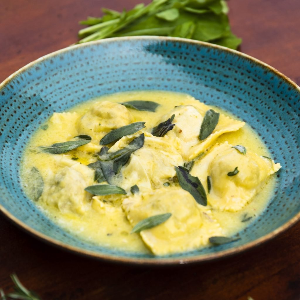 primer-plano-de-deliciosa-pasta-de-ravioles-decorar-con-hojas-de-albahaca-sobre-mesa-de-madera