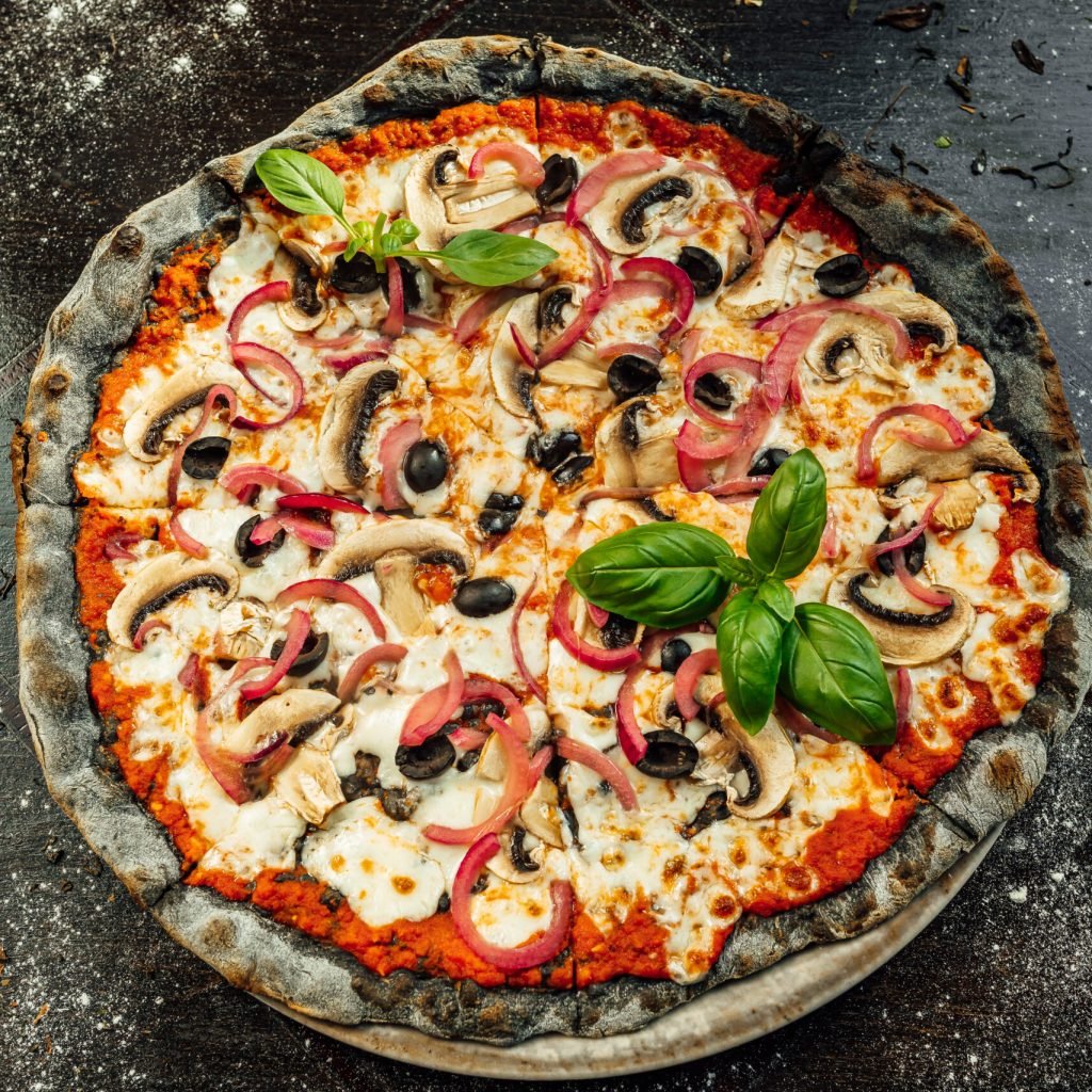 A top view of appetizing pizza with black dough and various vegetables